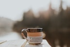 Steaming cup of coffee next to a tea pot on a wooden picnic table