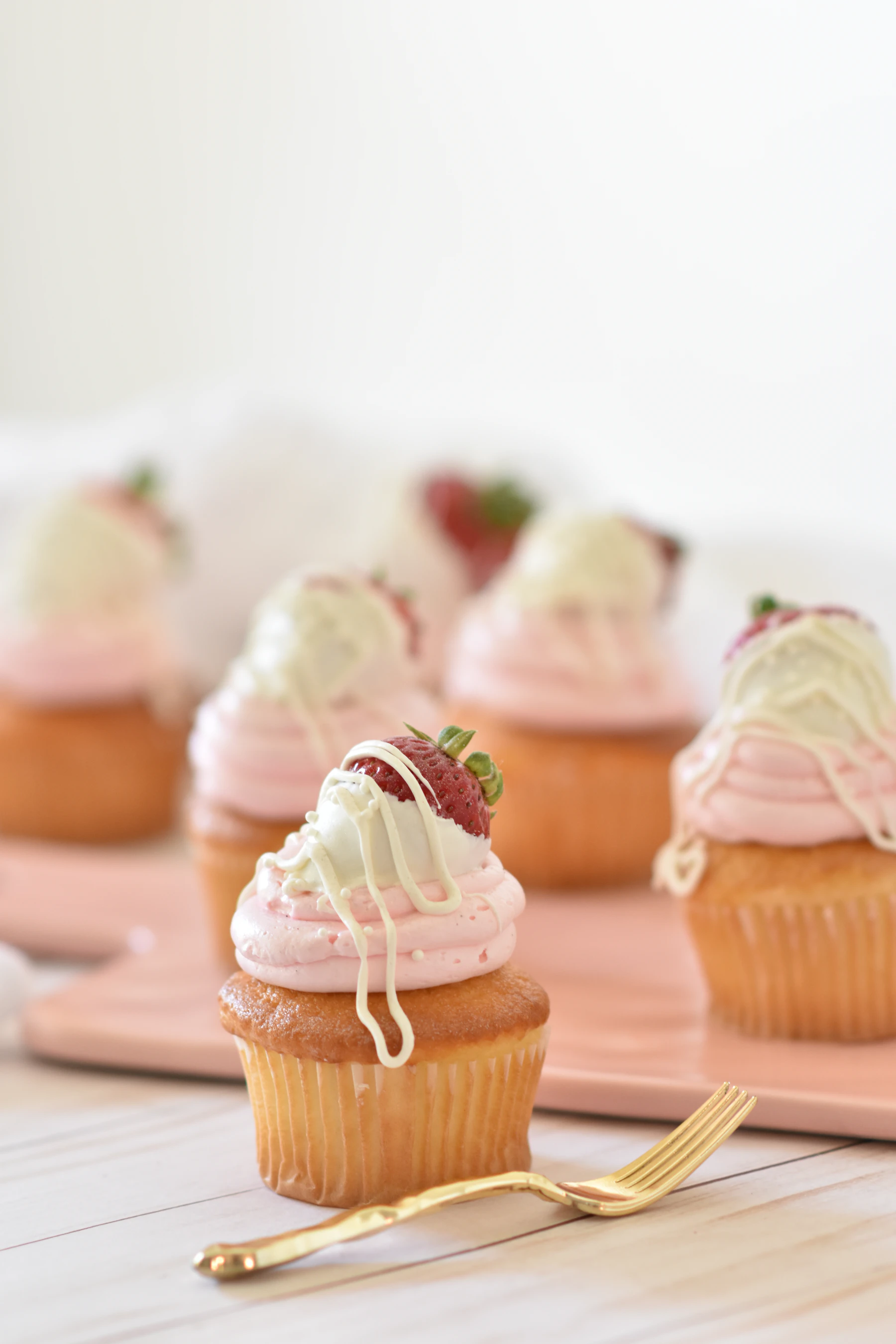 Vanilla cupcakes topped with pink frosting and strawberries on a pink tray