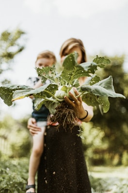 A proud woman holding a basket of fresh vegetables harvested from a local garden.