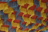 A ceiling decorated with alternating yellow and blue ruffled fabric, draped in a wave-like pattern against a warm, reddish-orange background. The fabric has a textured appearance with subtle sparkles scattered throughout, adding a festive and vibrant atmosphere.