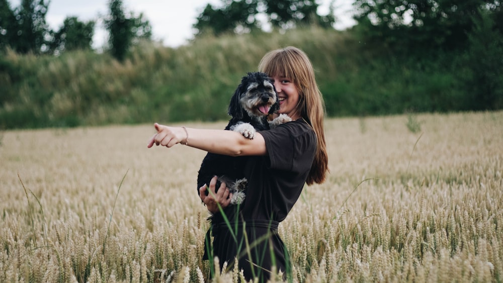 Frau steht auf Graswiese, während sie Hund hält