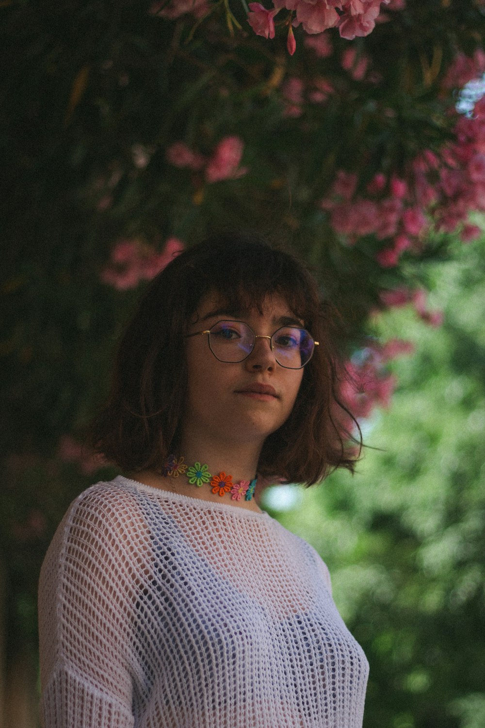 woman in white see-through blouse under the tree with pink flowers