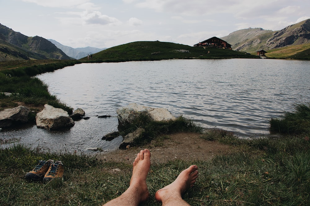 barefooted person lying on grass viewing lake and mountain
