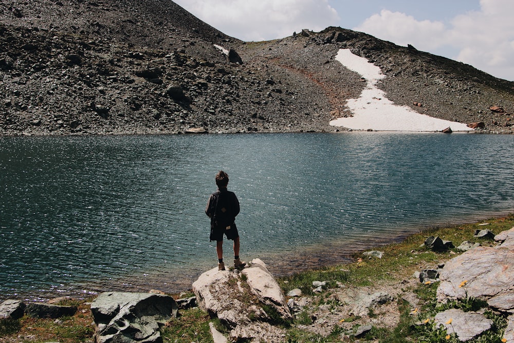 pessoa em pé na rocha ao lado do corpo de água durante o dia