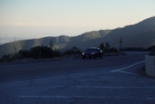 A scenic road winding through mountains with a car driving along it.