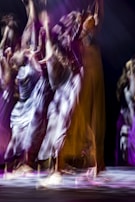 A dynamic scene with blurred figures in motion, suggesting a dance performance. The image captures the fluidity and energy of movement, with colors blending softly into each other.
