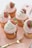 Five cupcakes are arranged on a light pink tray. Each cupcake is adorned with a swirl of pink frosting, topped with a fresh strawberry dipped in white chocolate and stylishly drizzled with additional white chocolate. A small golden fork accompanies the setup, enhancing the elegance and gourmet appeal.