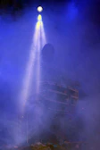 Drummer's silhouette pounding behind a veil of drifting fog and colored lights.