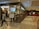A shopping mall hallway with a cafe on the left named 'Tea Trails Dining Tea Cafe' with a digital sign displaying 'Choco Kulcha'. People are visible inside the cafe and some sitting by the glass walls. A man and a young girl are walking in the foreground. On the right side, there is a ticket booth with people queueing.