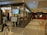 A shopping mall hallway with a cafe on the left named 'Tea Trails Dining Tea Cafe' with a digital sign displaying 'Choco Kulcha'. People are visible inside the cafe and some sitting by the glass walls. A man and a young girl are walking in the foreground. On the right side, there is a ticket booth with people queueing.