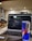 A laptop displaying code on its screen, set on a table in a modern, well-lit cafe. An open can of Red Bull energy drink is placed prominently next to the laptop. In the background, there are chairs and decorative wall posters.