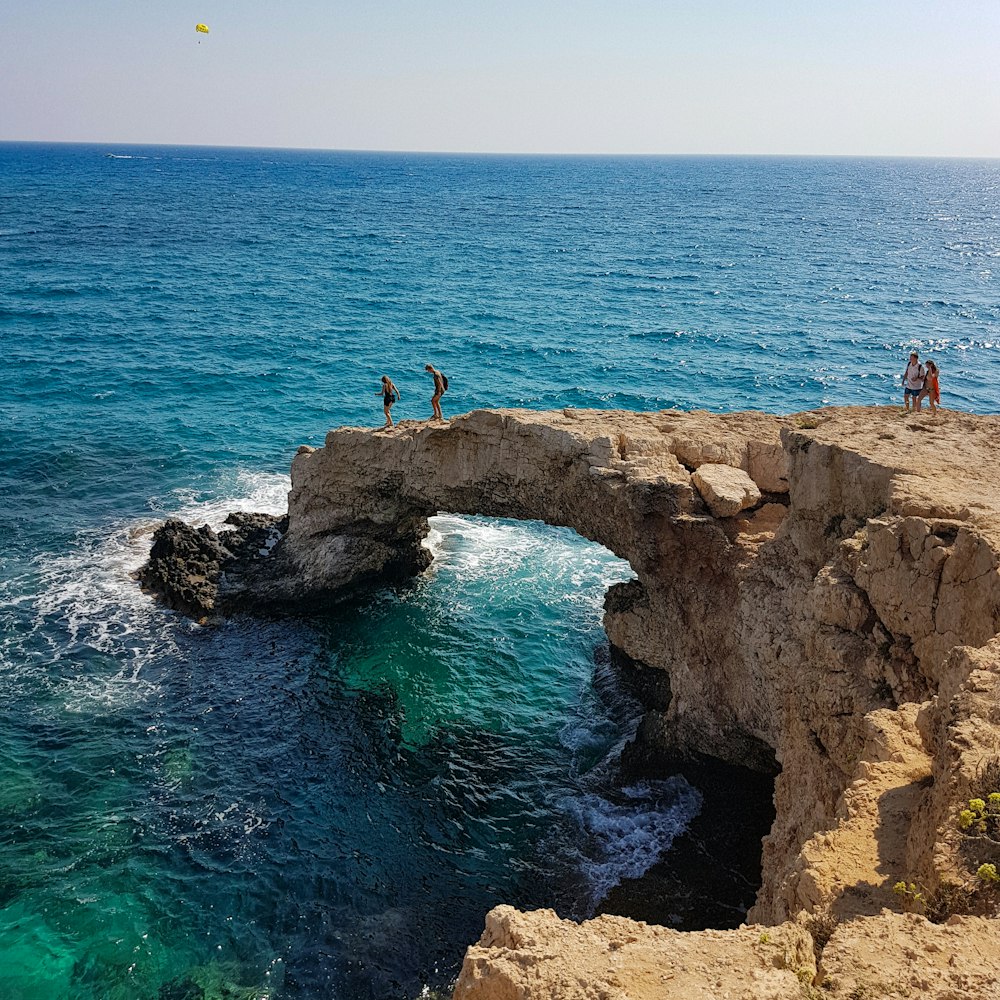 people standing on brown cliff beside ocean