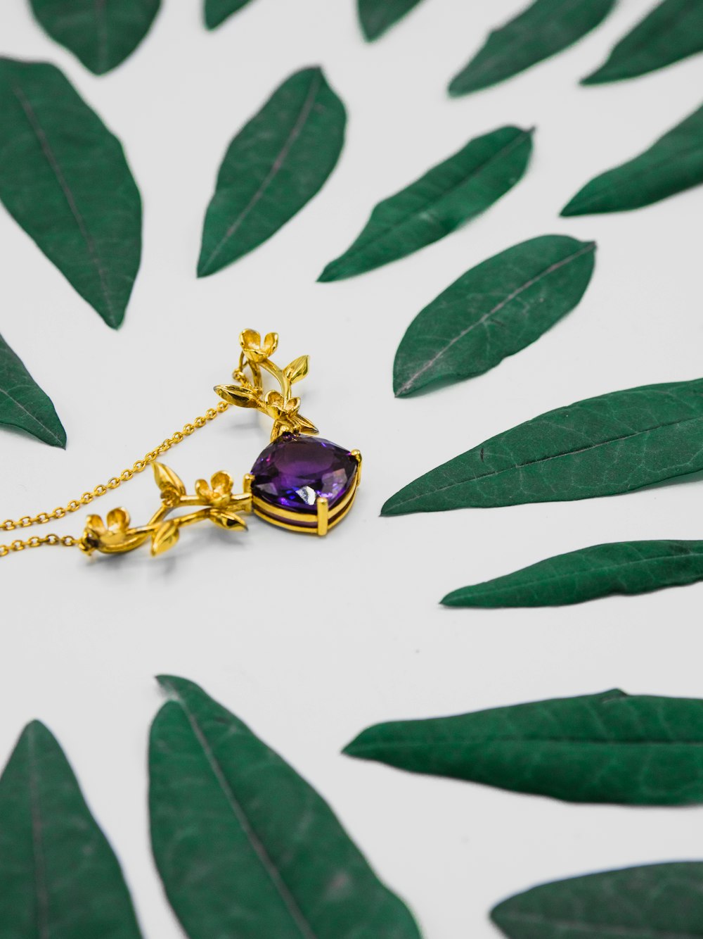 gold-colored pendant with purple stone besides green leaves