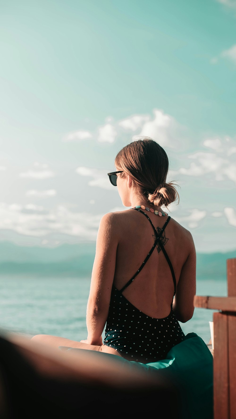 mulher usando monokini sentada no assento verde de frente para o oceano