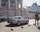 Smiling young man holding car keys next to a rental car in an Italian city.
