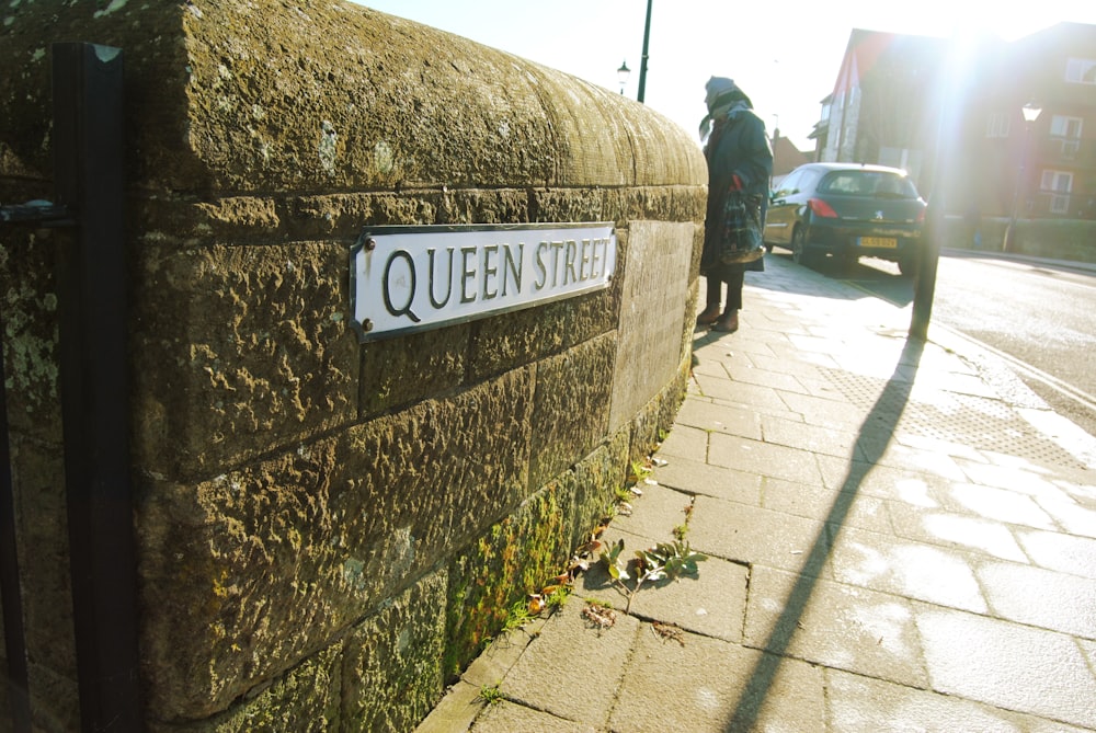 white and black Queen Street sign on gray concrete wall