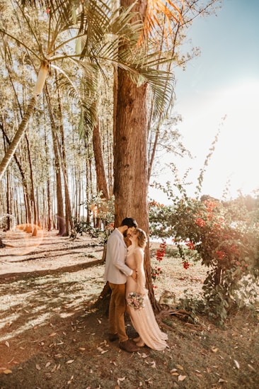 man and woman standing close and facing each other beside tall tree