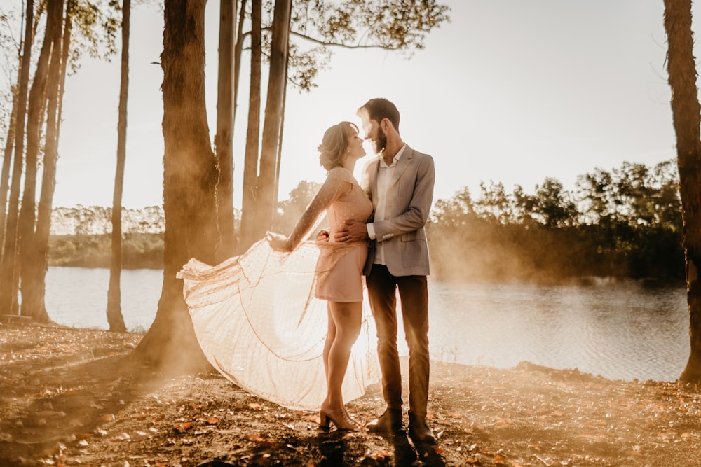 standing man and woman beside trees near body of water