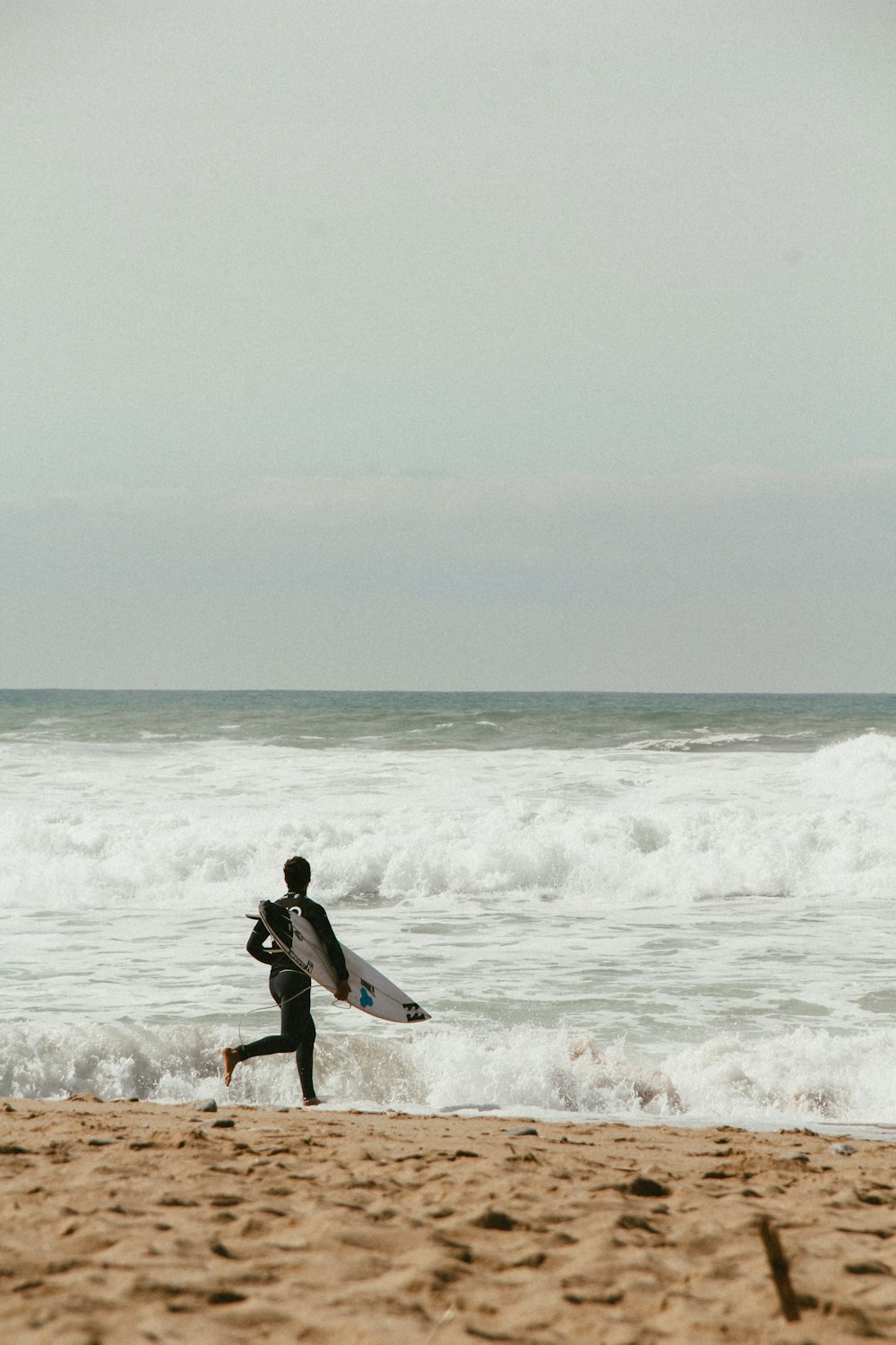 man running towards the shore carrying surfboard