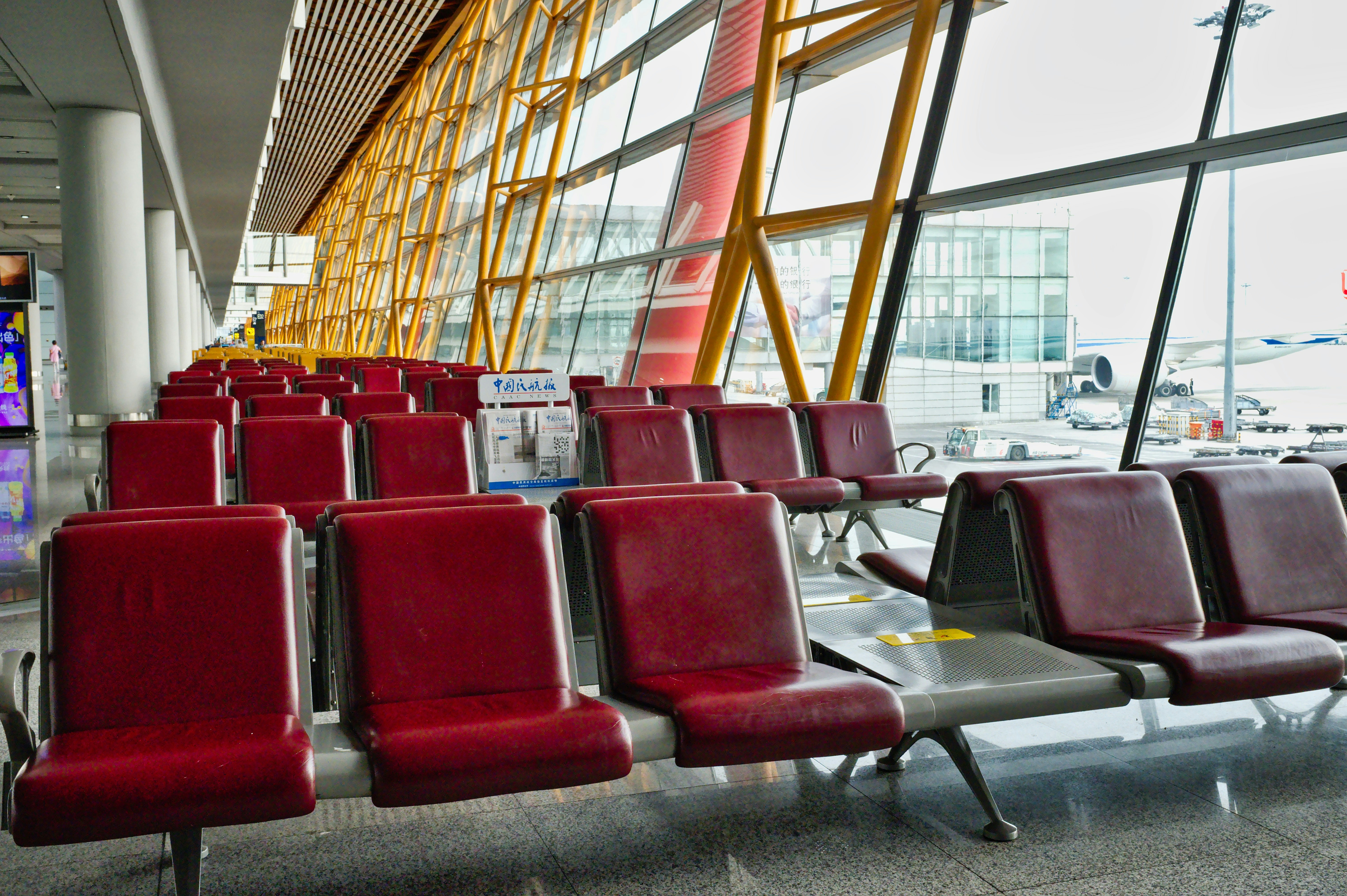 red gang chair, Modern Airport Interior Featuring Empty Red Seating Areas With Large Windows on a Cloudy Day - The terminal showcases a spacious area filled with red seating, designed for travelers waiting for their flights. Large windows allow natural light to illuminate the surroundings while offering views of the aircraft outside. The architecture highlights a contemporary design with vibrant colors.