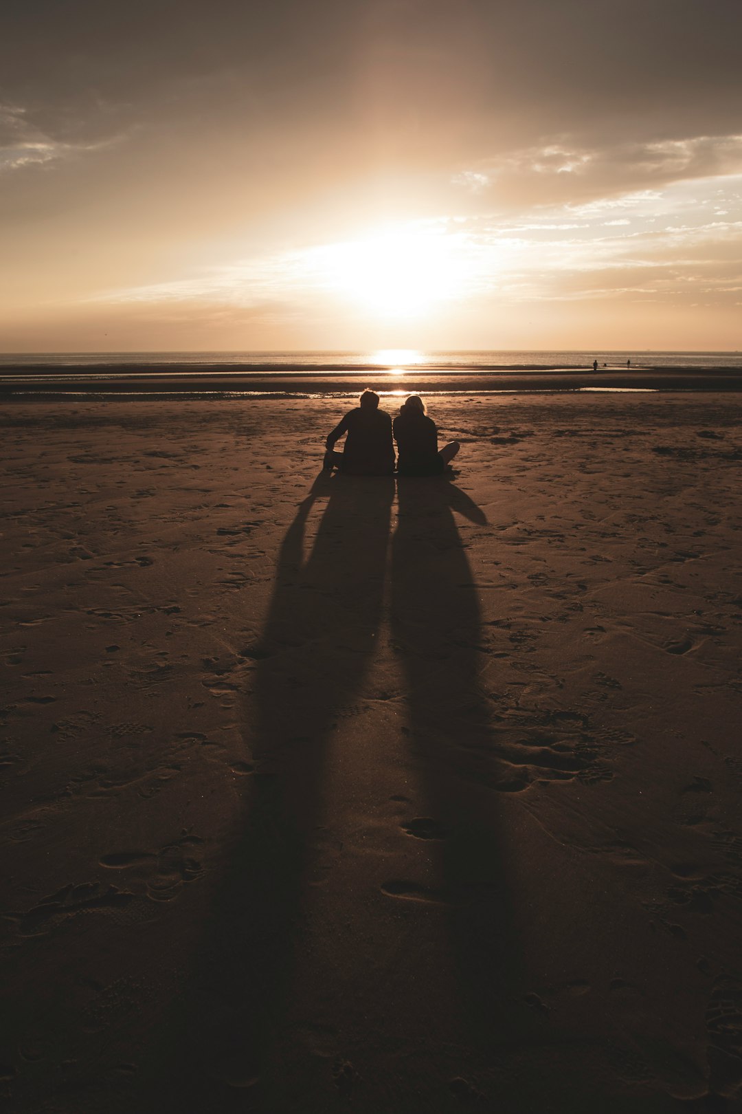 silhouette photography of two people sitting by the beach during golden hour