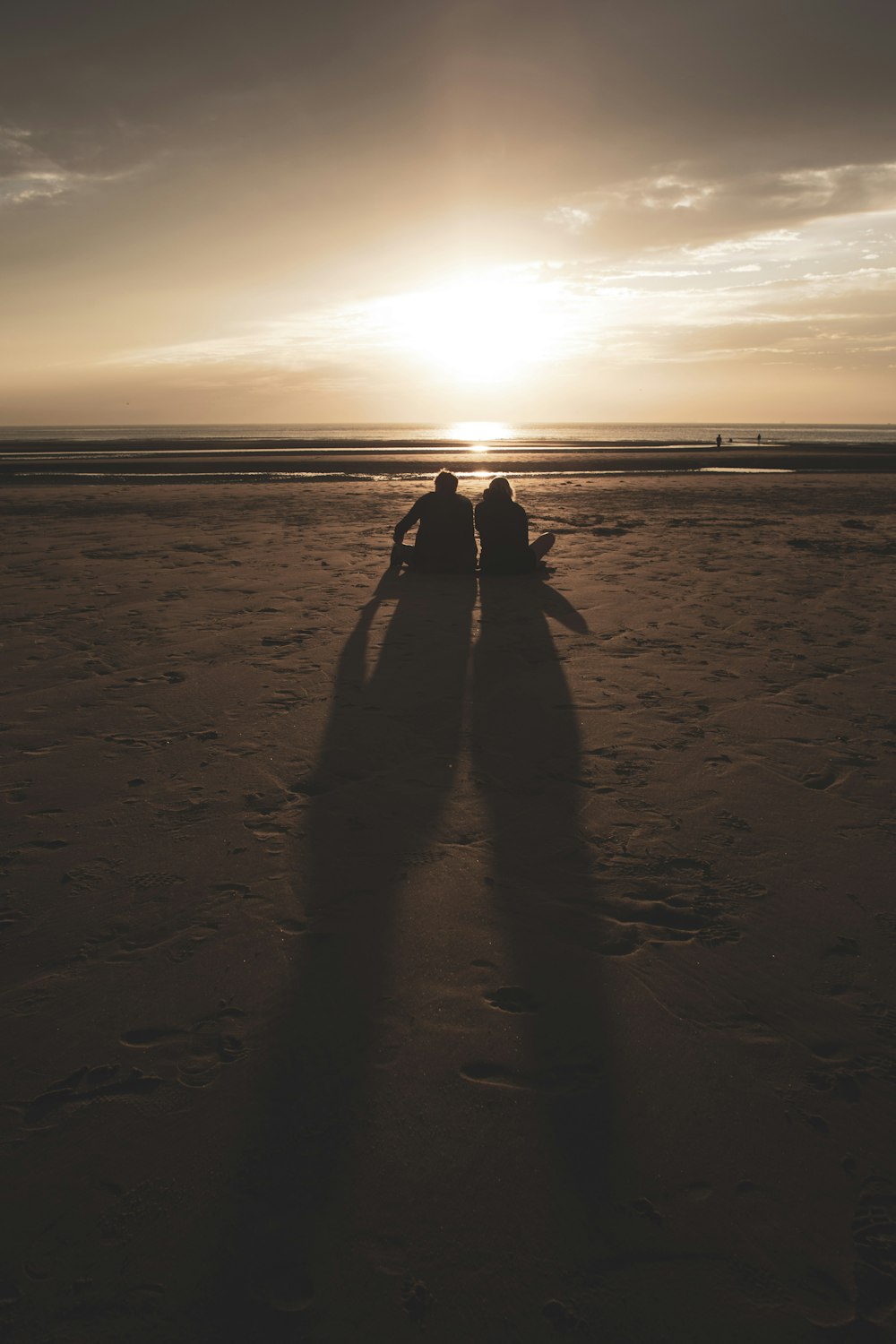 silhouette photography of two people sitting by the beach during golden hour