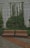 Two wooden benches with black metal frames are placed on a tiled pathway, surrounded by lush green foliage and climbing plants on a large concrete wall.