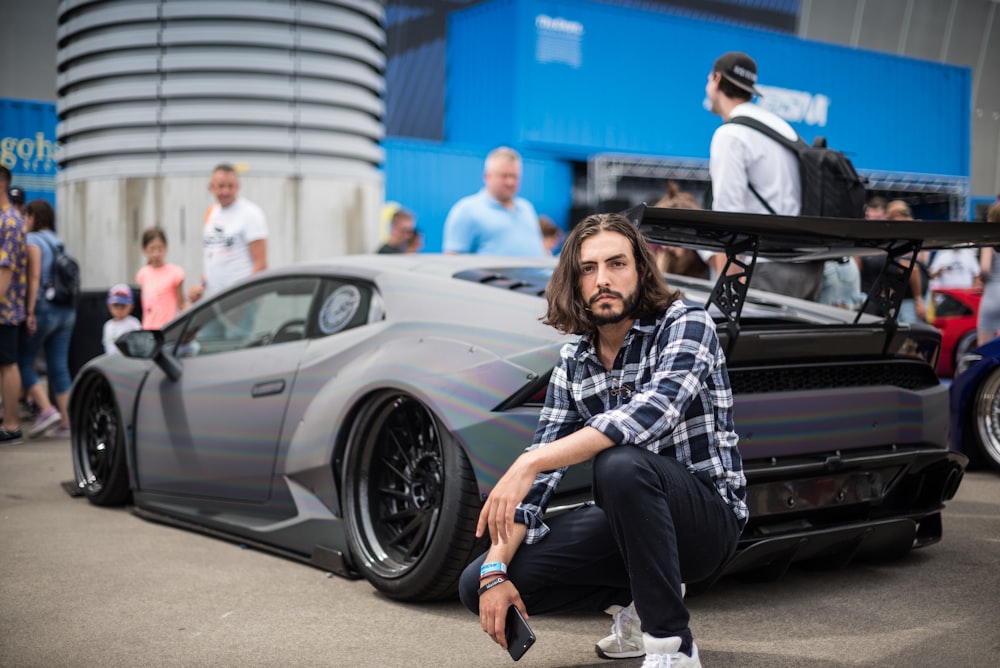 man sitting beside sports coupe