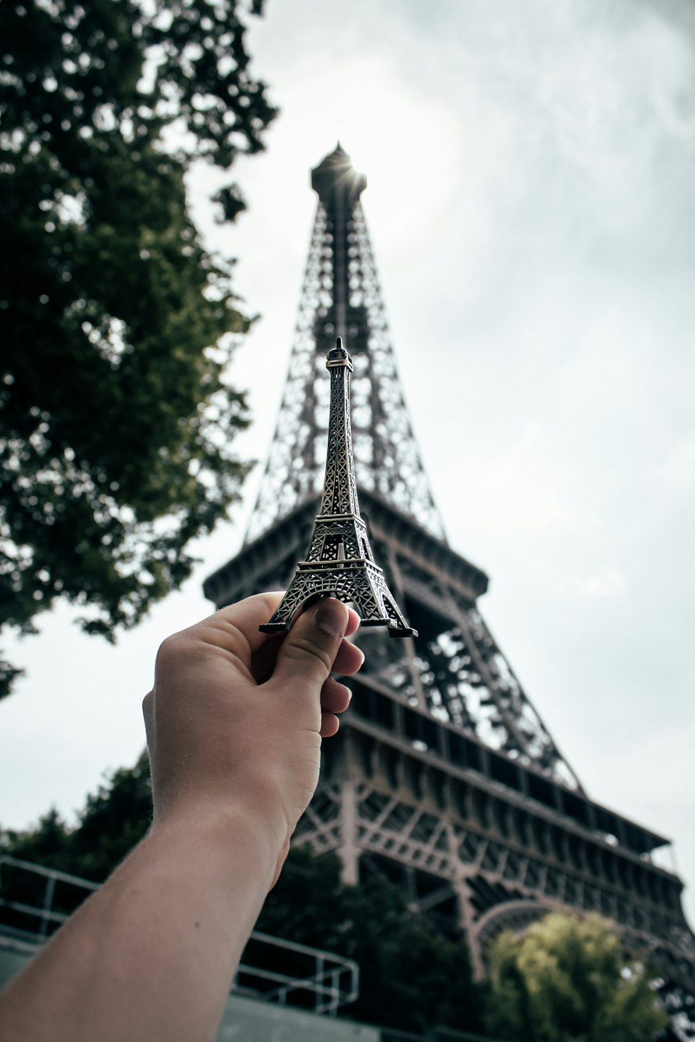 Person, die einen Mini-Eiffelturm hält und ihn mit dem echten Eiffelturm vergleicht