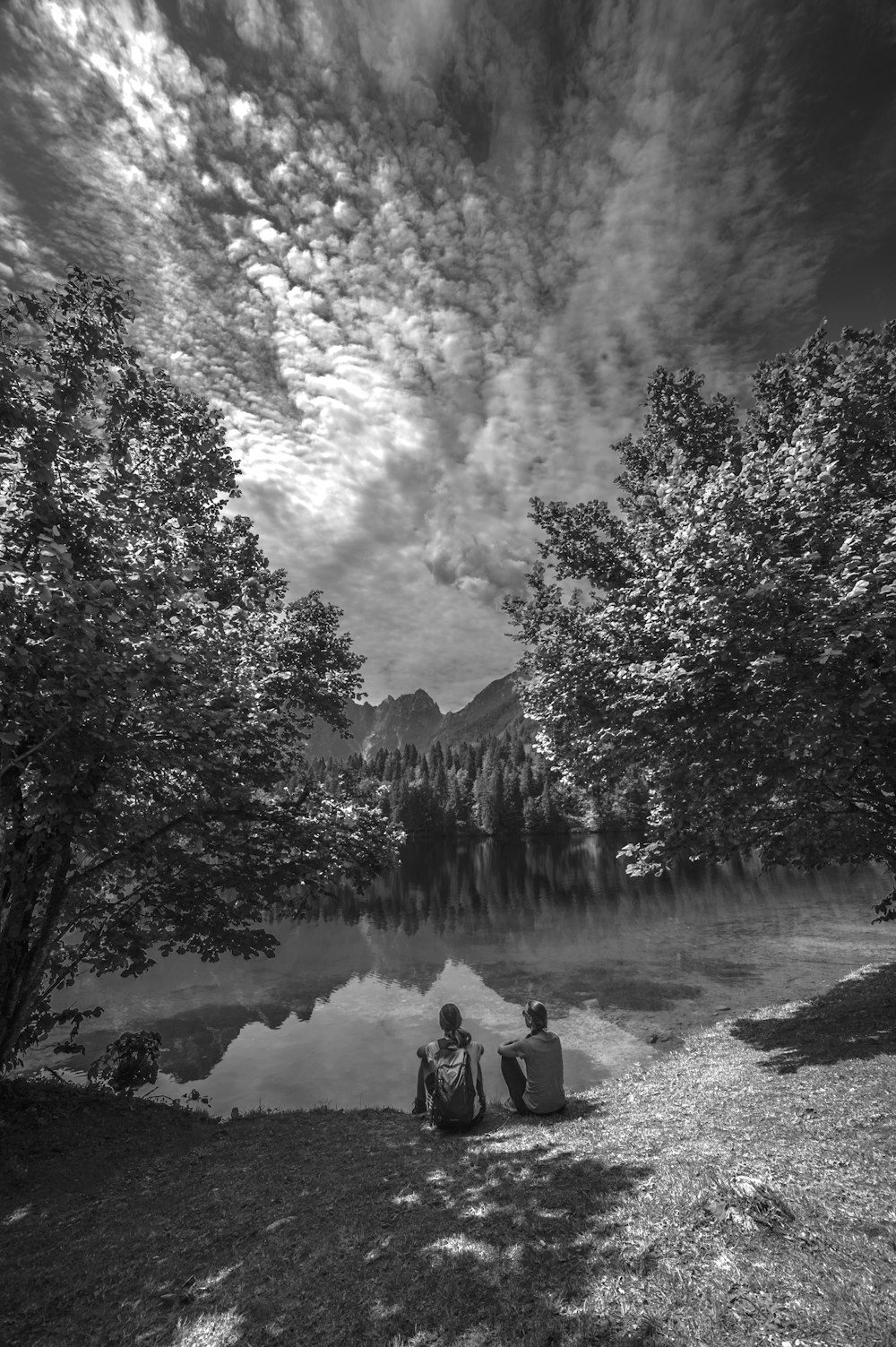 two person sitting near body of water during daytime grey-scale photography