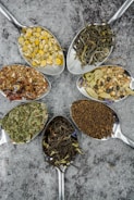 seven different spices and herbs on gray stainless steel spoons