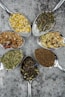 seven different spices and herbs on gray stainless steel spoons