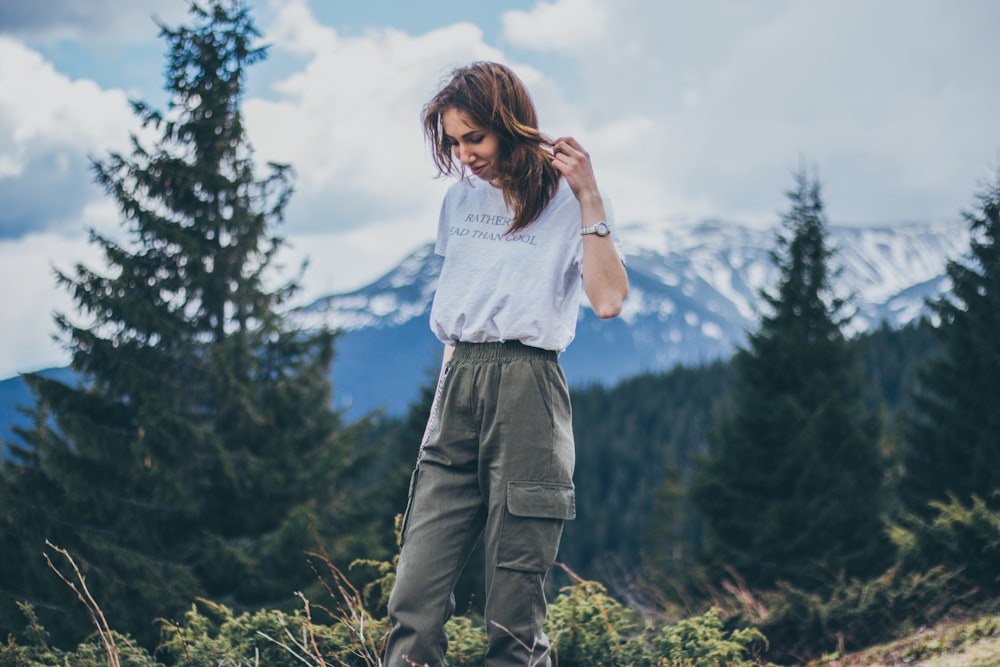 woman in grey shirt and green cargo pants standing on mountain top
