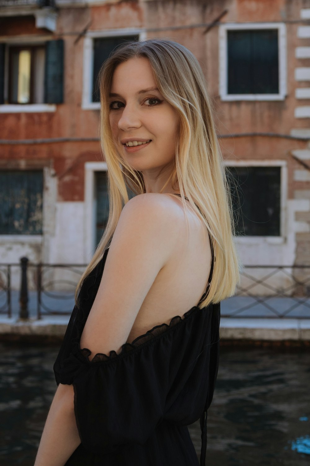 woman in black off shoulder dress standing near canal