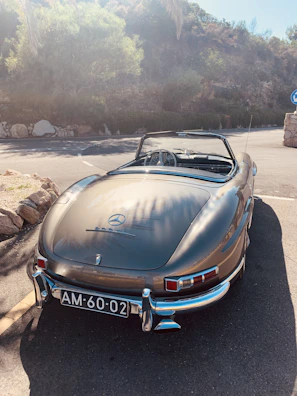 Vintage Mercedes Benz driving on a scenic road, sunlight reflecting off its shiny surface