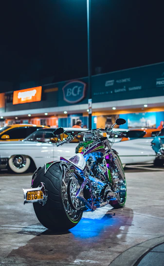 A neon-lit street at night with a custom modified bike parked under electric blue and safety orange lights.