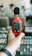 A hand holds a red sound level meter with a digital display reading 00.7. The background is blurred, suggesting an indoor environment, possibly with audio equipment nearby.