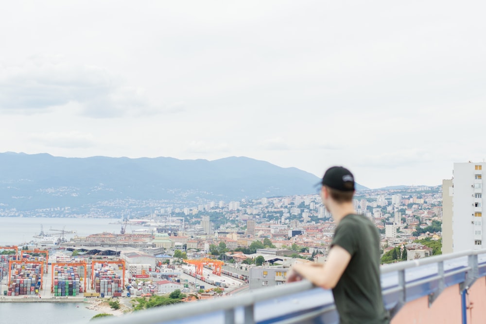 man standing on railing overlooking city buildings