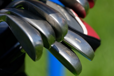 Close-up of modern golf equipment laid out neatly on a wooden table with a golf course background.