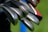 Close-up view of several golf clubs with metal heads, arranged in parallel. The background includes shades of green and hints of blue and red colors.