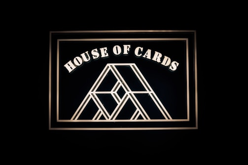 A geometric design resembling a house of cards is framed against a dark background. Bold, white lettering spells out 'House of Cards' above the central illustration.