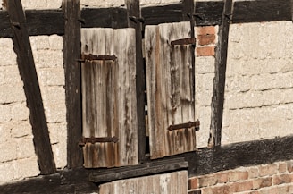 A close-up of weathered colonial-era wooden window shutters bathed in soft morning light.