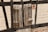 A close-up of a weathered wooden window shutter mounted on a rustic wall. The wall is partially constructed from dark wooden beams and light-colored bricks. The shutter has a rough, aged texture with visible knots and cracks in the wood.