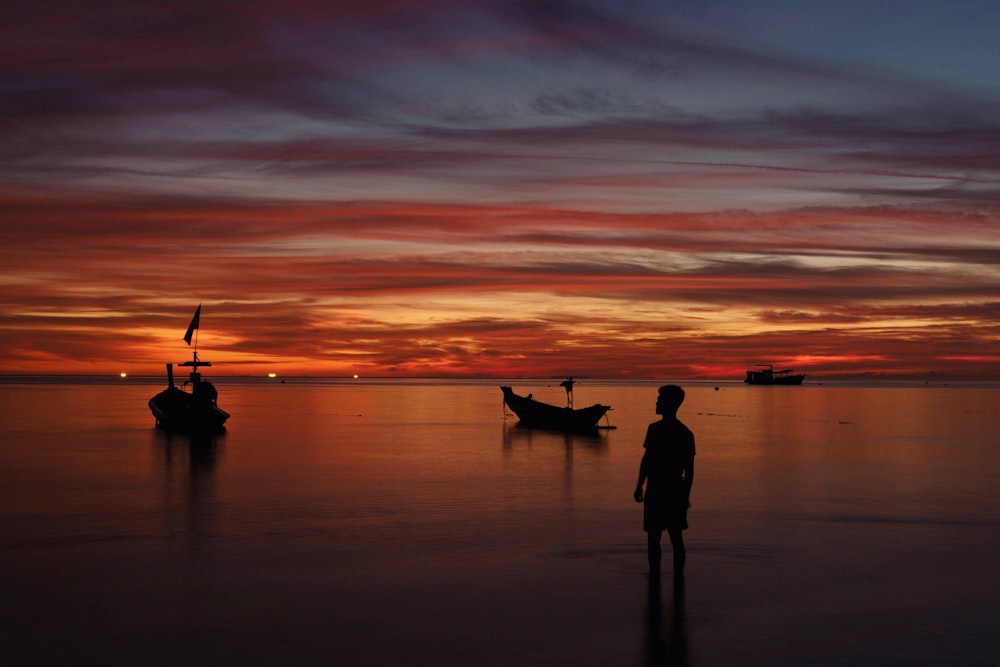 person standing near in water near boats during golden hour