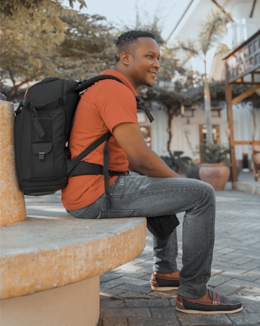 A happy traveler sitting on a bench in a bustling city park, the backpack resting beside them.