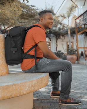 A college student laughing casually while seated on a stone wall at a campus park.