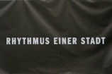Text in bold white letters reads 'RHYTHMUS EINER STADT' on a dark background that appears textured or slightly crumpled.