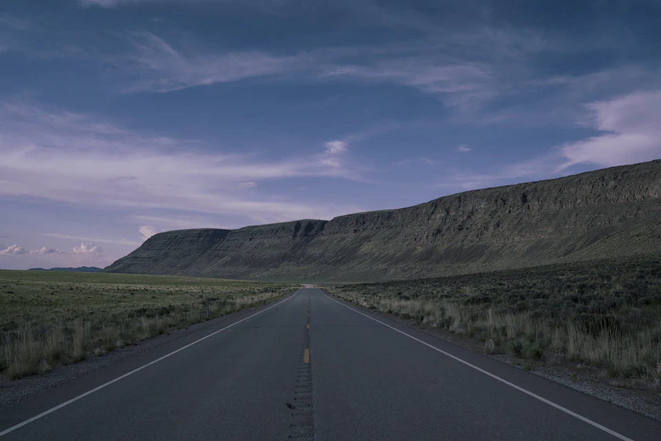 Long, straight road cuts through desert landscape, stretching towards distant mountain range