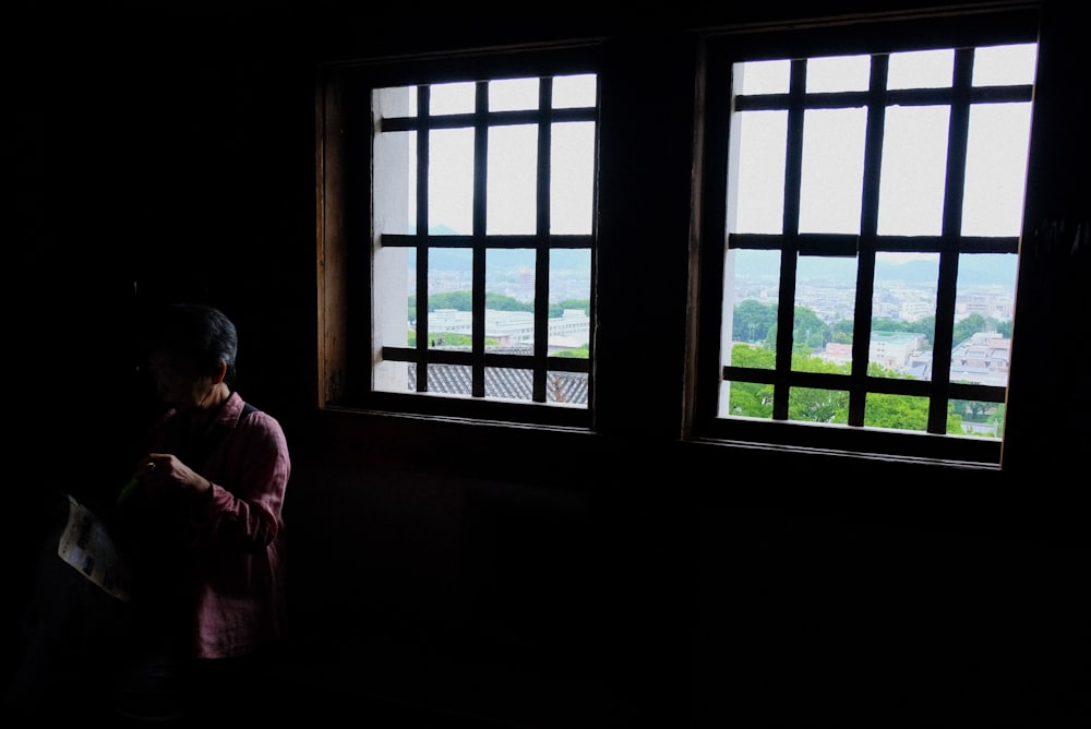 a woman standing next to two windows in a dark room