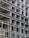 A building under construction with a visible concrete frame and multiple rectangular openings arranged in a grid pattern. The structure appears unfinished, showing bare concrete surfaces and metal rods.
